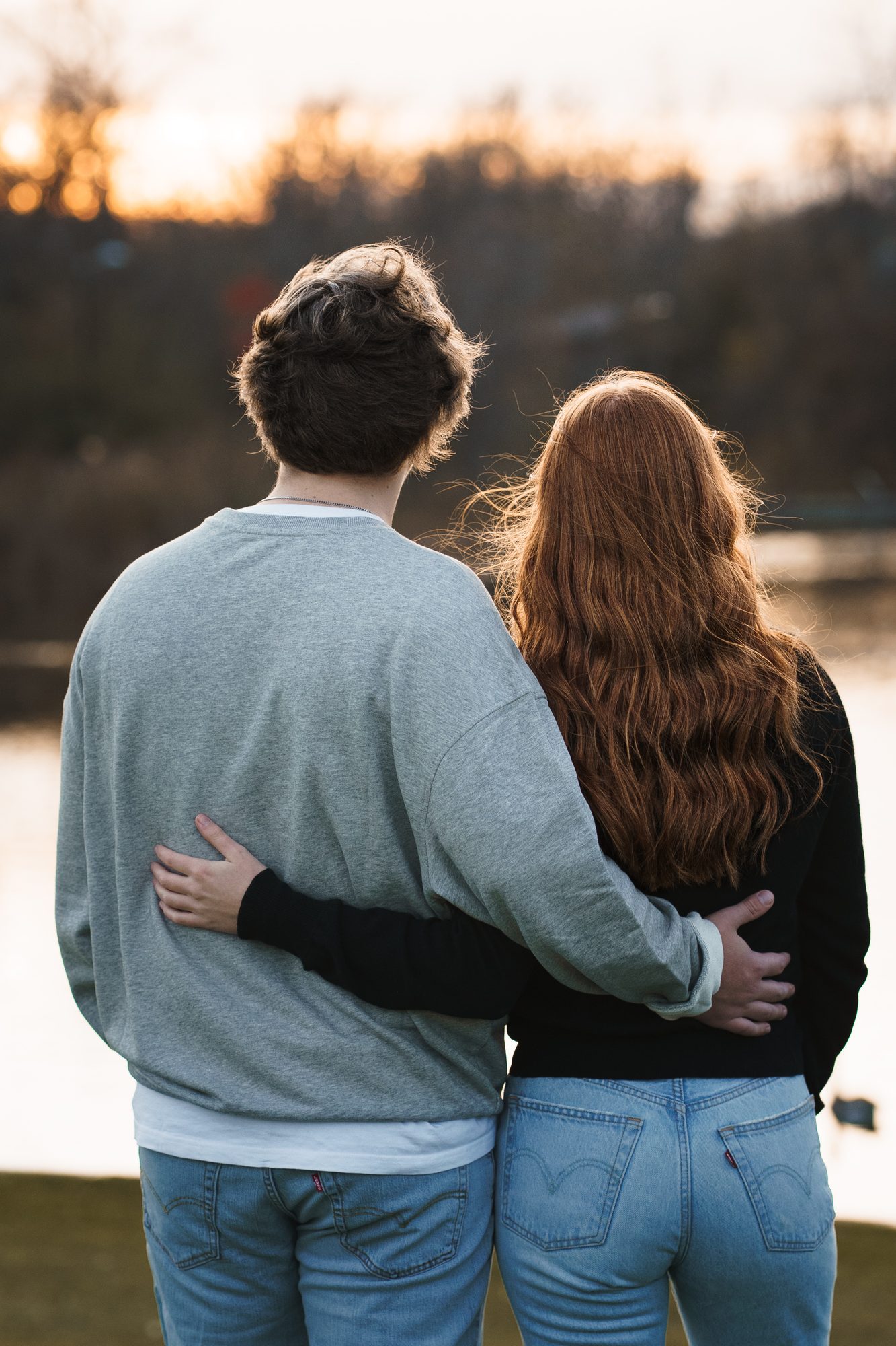 Couple with arms around each other looking out over the river at sunset, Winnipeg engagement session