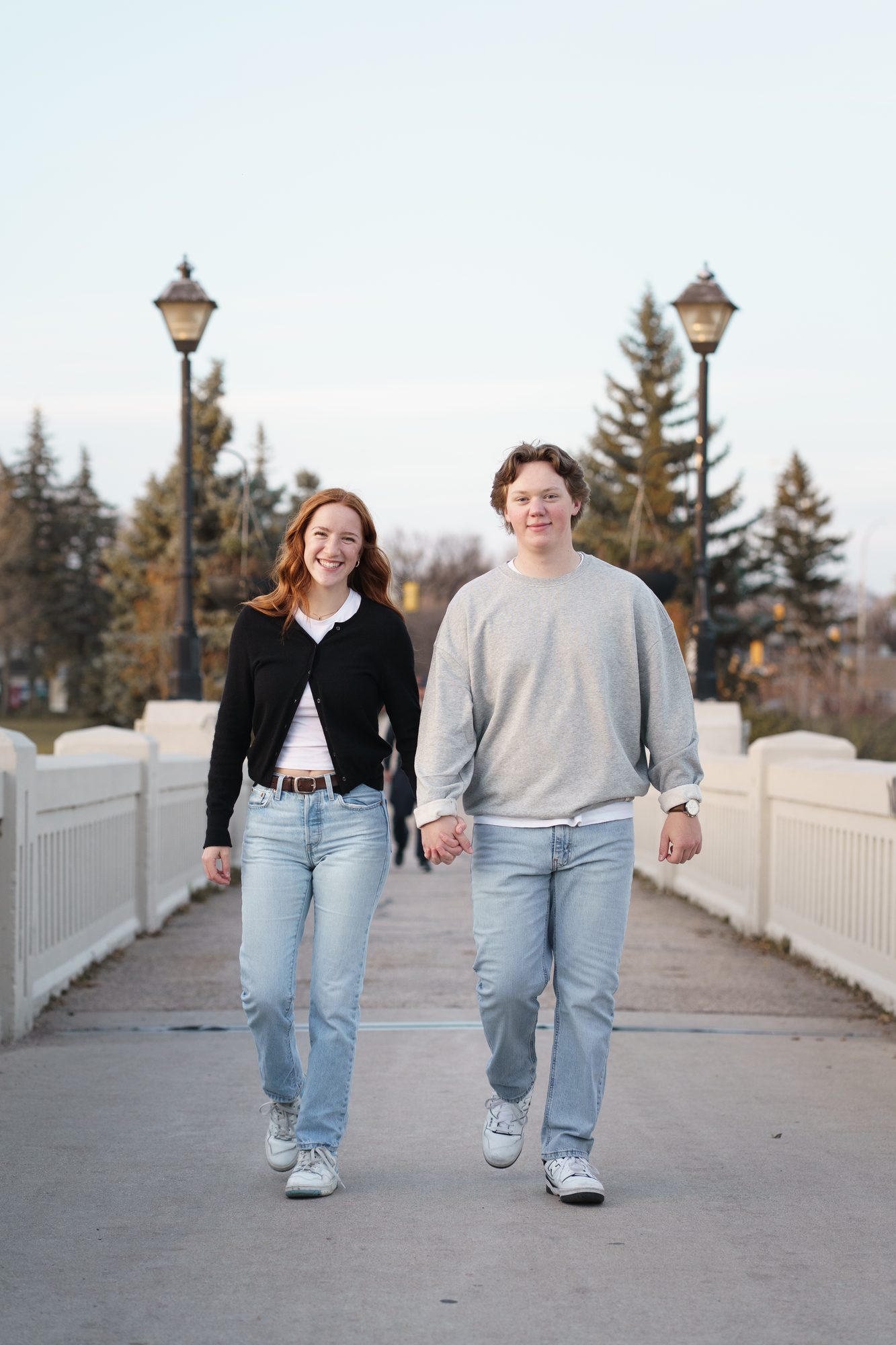 Couple walking hand in hand across a white footbridge during an engagement session in Winnipeg