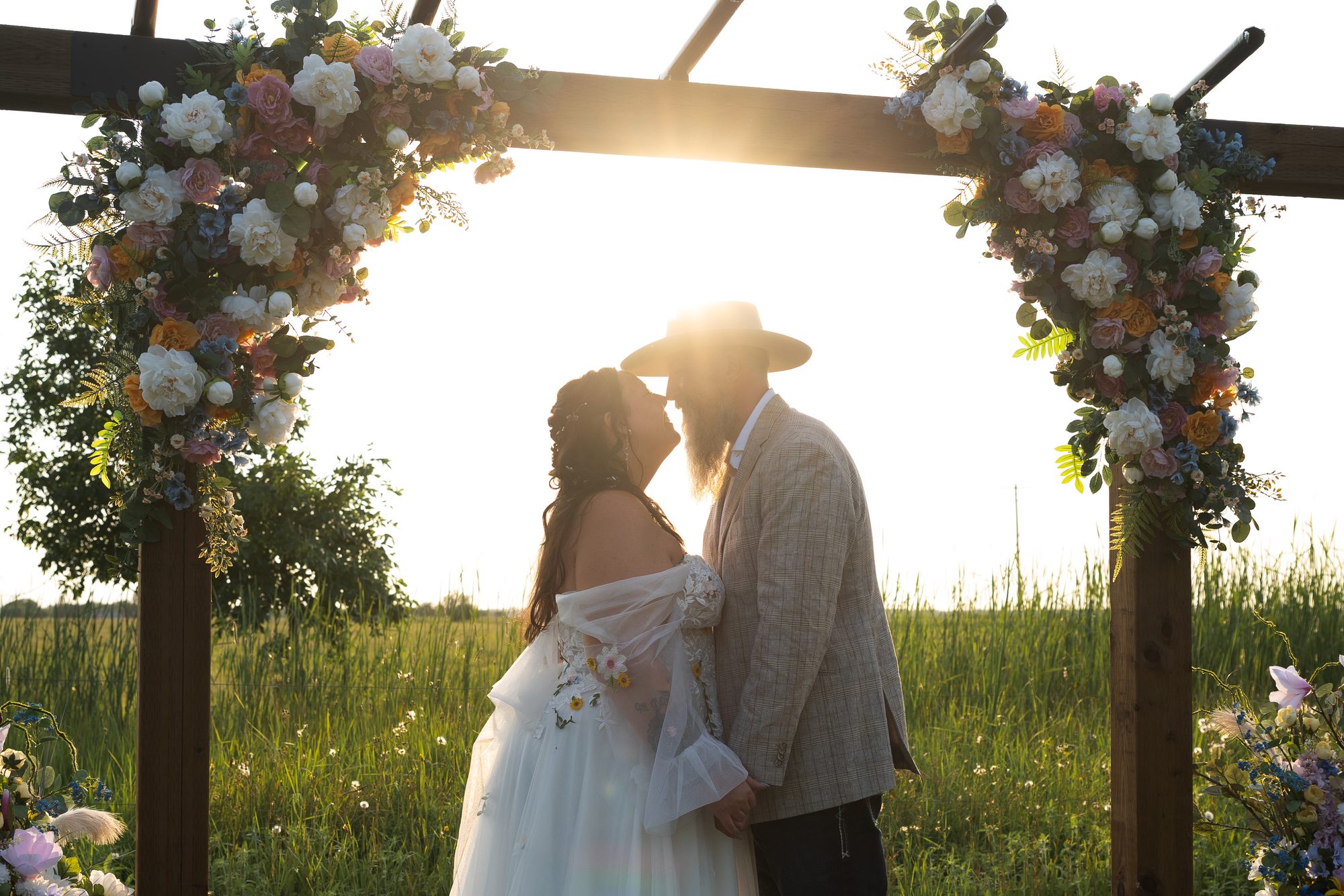 Bride and groom about to kiss under a floral arch at sunset at an outdoor Manitoba wedding