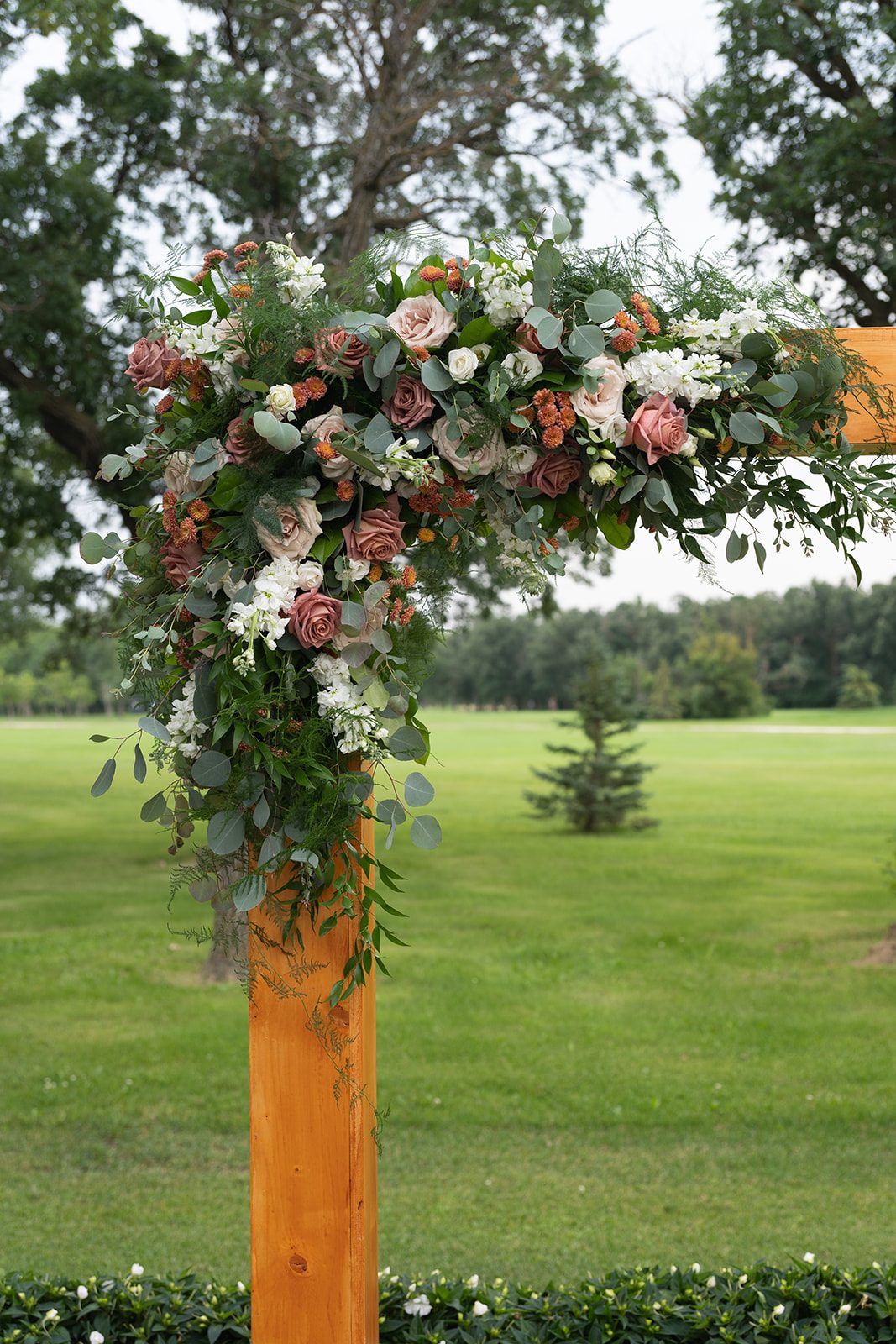Floral arrangement on the ceremony arch with the golf course behind it at Breezy Bend Country Club